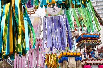 青や緑紫や金など様々な色と素材の七夕飾りが空中に吊るされているにぎやかなお祭り風景を捉えています