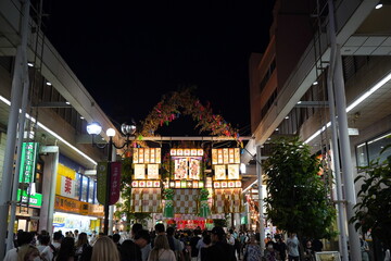 夜の商店街に大勢の人が集まりライトアップされた豪華な七夕飾りの下を歩く賑やかな夏の祭りの光景です