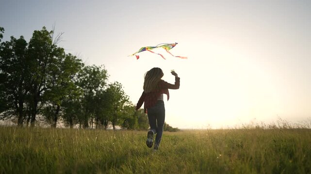 Running with kite across meadow field, girl jump and run through tall grass at sunset, rainbow kite trailing ribbon, nature summer outdoors atmosphere, playful energy and sense of freedom and movement