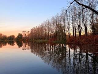 Fototapeta premium autumn trees silhouettes reflection on the still lake surface, twilights time, natural sky colors after the sunset