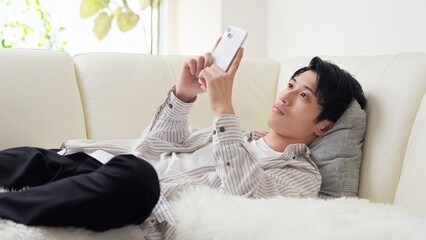 寝ながらスマホを見るアジア人男性