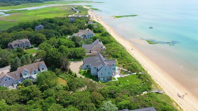 High aerial perspective of a sandy shoreline where families relax under umbrellas, children splash in shallow surf, and boats drift across calm turquoise waters beneath summer skies.