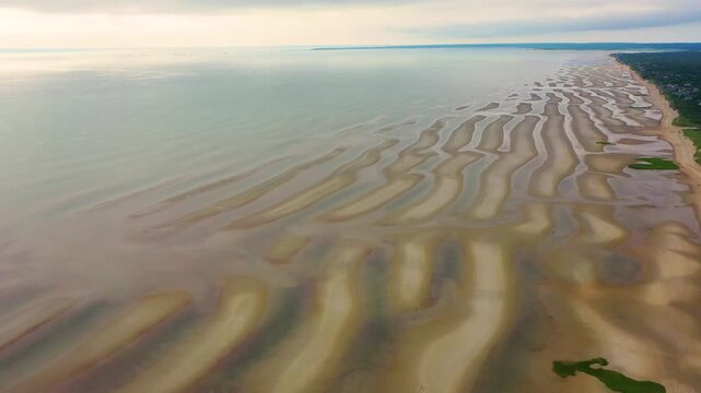 Cape Cod shoreline at low tide with rows of beach houses sitting above sandy bluffs, shimmering tide pools dotting the exposed flats, and dense greenery extending inland toward the horizon.