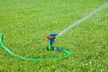 Plastic irrigator in a fresh green mowed lawn with green plastic pipe