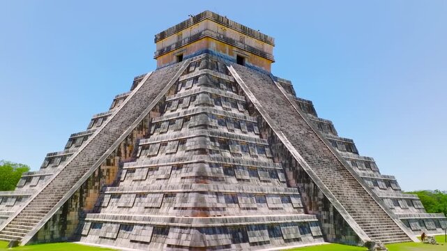 Stone pyramid with wide stairs, clear blue sky backdrop. Lush trees surround the base