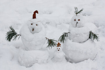 A family of snowmen against the background of the snow. Two large snowmen and one small snowman are standing in a clearing in the snow. High quality photo © Лариса Прокопова