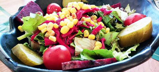 Mix of fresh organic juicy salad greens and red and yellow cherry tomatoes in grey plate on rustic wooden table. Food photography
