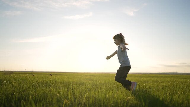 girl running through green grass in open field under bright sun and blue sky silhouette against glowing horizon while child play in meadow with gentle breeze and joyful movement and child smile