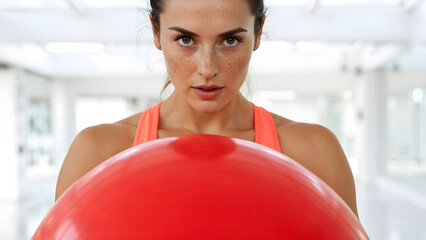 Focused woman holding a red exercise ball, preparing for a workout session in the gym