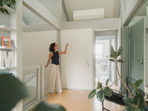 Woman using remote control for air conditioning at home in summer