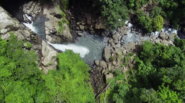 Aerial view of the Tomagelli Waterfall as it cascades down rugged rocks into a serene pool surrounded by lush green vegetation, Barru, Sulawesi Selatan, Indonesia.