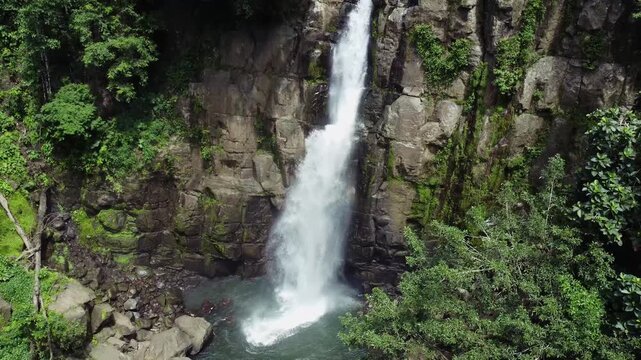 Aerial view of the majestic Tomagelli Waterfall cascading powerfully down the rocky cliffside into the pool below, surrounded by lush greenery, Barru, Sulawesi Selatan, Indonesia.