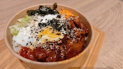 Korean rice bowl with spicy chicken, fried egg, and fresh vegetables topped with sesame