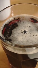 Close-up of a dark beer in a glass with foam on top and warm light reflections