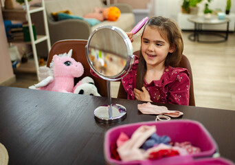 Little girl enjoys grooming her hair while seated at a cozy table adorned with colorful accessories...