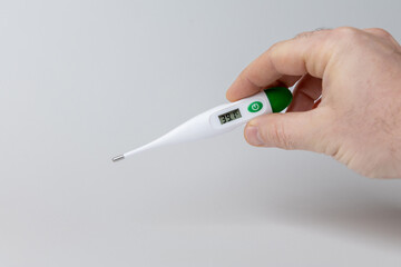 Hand holding digital thermometer displaying temperature reading of 37.4 degrees Celsius against a minimalistic background, emphasizing health monitoring and wellness awareness