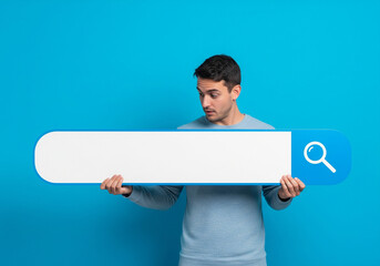 A man holding a large horizontal search bar with a magnifying glass icon on one end, standing against a bright blue background. The man looks down curiously at the blank search bar.
