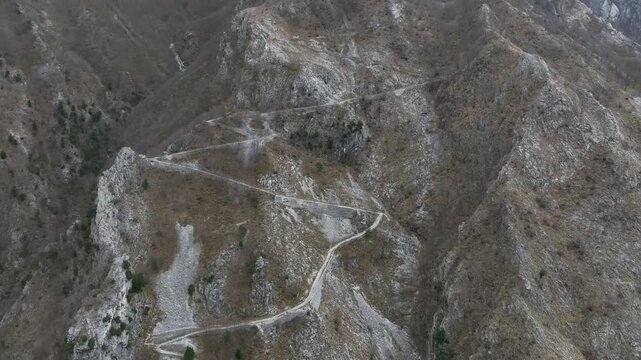 Aerial view of a serpentine road snaking through the rugged, bare mountains, showcasing the contrast between the man-made path and nature, Resceto, Tuscany, Italy.