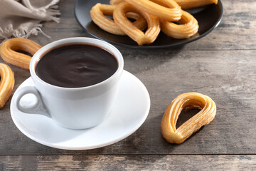 Hot thick chocolate in a white cup with churros on wooden table