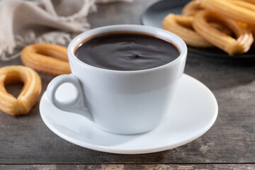 Hot thick chocolate in a white cup with churros on wooden table