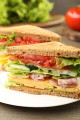 Tasty sandwiches with ham, cheese and vegetables on wooden table, closeup