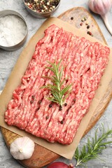 Raw minced meat with rosemary and spices on grey textured table, flat lay