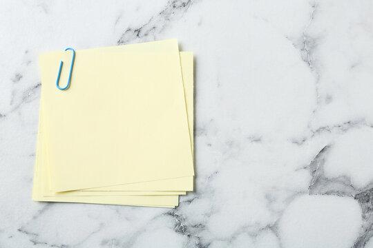 Blank yellow notes with paper clip on white marble table, top view. Space for text