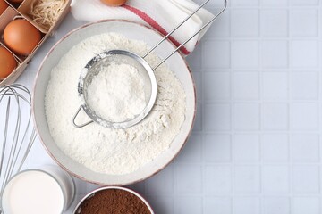 Ingredients for dough, whisk and strainer on white tiled table, flat lay. Space for text