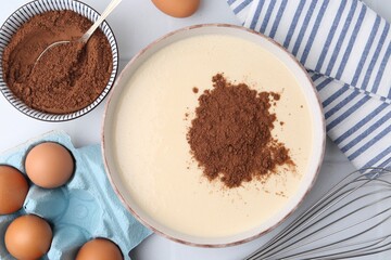 Adding cocoa powder into bowl with dough at white table, flat lay