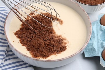 Adding cocoa powder into bowl with dough at white table, closeup