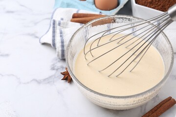 Liquid dough in bowl, whisk and ingredients on white table, closeup. Space for text