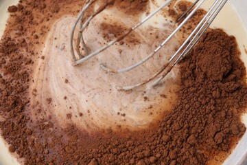 Adding cocoa powder into bowl with dough, closeup