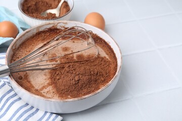 Adding cocoa powder into bowl with dough at white tiled table, closeup. Space for text