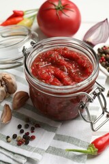 Tasty salsa sauce in jar and ingredients on white wooden table, closeup