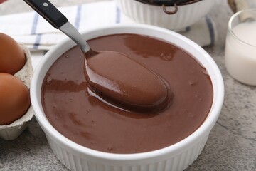 Taking liquid chocolate dough from bowl with spoon on grey table, closeup