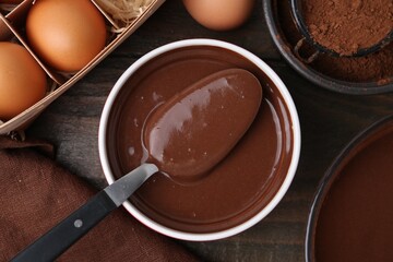 Liquid chocolate dough in bowl and ingredients on wooden table, flat lay