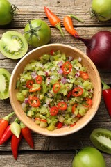 Tasty salsa in bowl and ingredients on wooden table, flat lay