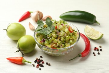 Tasty salsa in bowl and ingredients on white wooden table, closeup