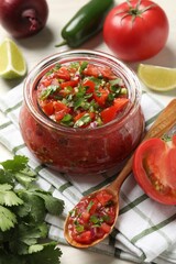 Tasty salsa in jar and ingredients on white table, closeup