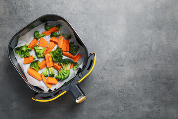Grilled vegetables in air fryer basket on grey table, top view. Space for text