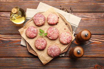 Raw meat patties with parsley and peppercorns on wooden table, flat lay