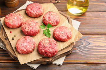 Raw meat patties with parsley and peppercorns on wooden table, closeup. Space for text