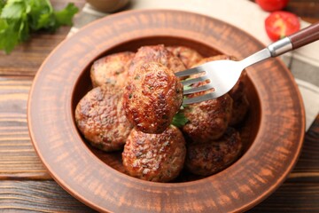 Taking roasted meat patty with fork at wooden table, closeup