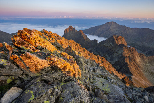 Aerial view of the jagged peaks of Maly Ladovy stit bathed in the warm glow of sunrise against the backdrop of a misty valley, Tatranska Javorina, Presov Region, Slovakia.