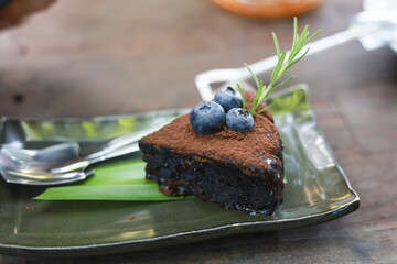 Delicious slice of dark chocolate cake on green plate. Decadent dessert topped with cocoa powder,...
