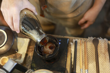 Focused barista pouring cold brew coffee from glass decanter into ceramic cup with ice. Artisanal preparation at cafe showing moment of calm concentration and skill