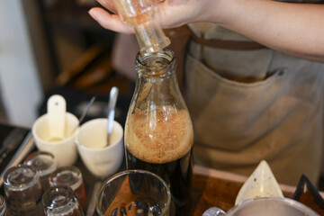 Professional barista pouring syrup into glass bottle, skillfully making specialty coffee drink. This focused beverage preparation inside cozy cafe shows craft process