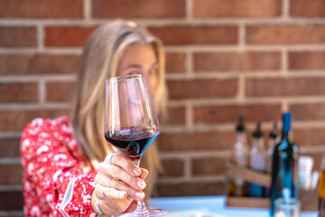 Happy blonde woman holding red wine glass close up focus on crystal glass cheers elegant lifestyle and joyful mood