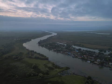 Aerial view of the winding, reflective river cutting through lush green landscapes and small villages at dusk, Bucharest, Romania.