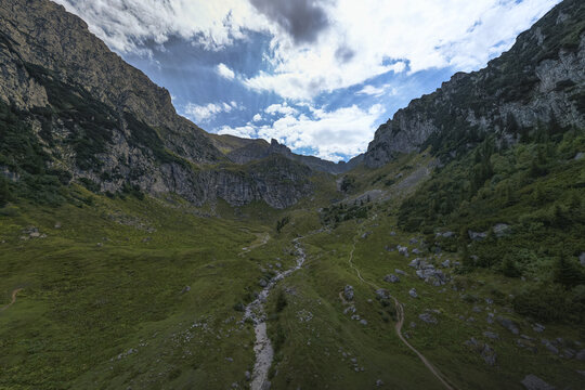 Aerial view of a valley carved by a stream, framed by rocky cliffs under a sky with scattered clouds, Bucharest, Romania.